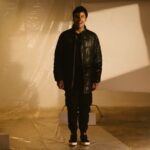 Chicco Jerikho tersenyum mengenakan jaket puffer hitam dan sepatu Ventela
